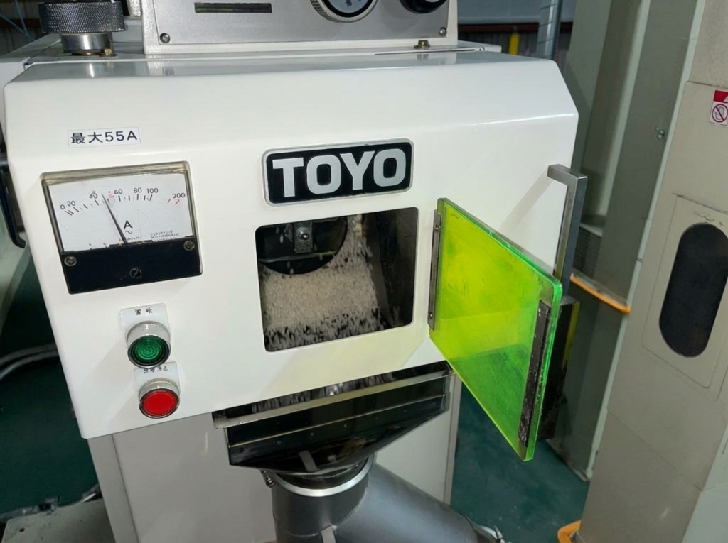 精米機の確認窓から搗精後の白米が流出している様子を確認し、砕米や過搗精の兆候を目視でチェックしている状況